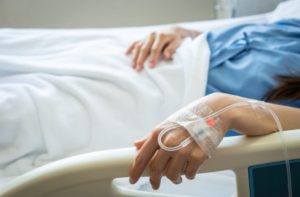 Patient woman sleeping with receiving intravenous fluid directly into a vein while her hand touching bed rails on hospital bed. stock photo