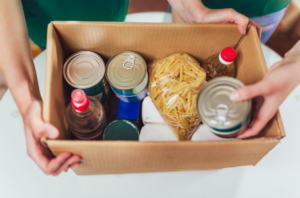 a cardboard box containing donated tinned and packet food is passed from one individual to another