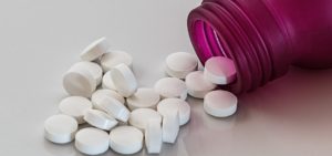 round white tablets shown spilling from a pink pill bottle onto a surface